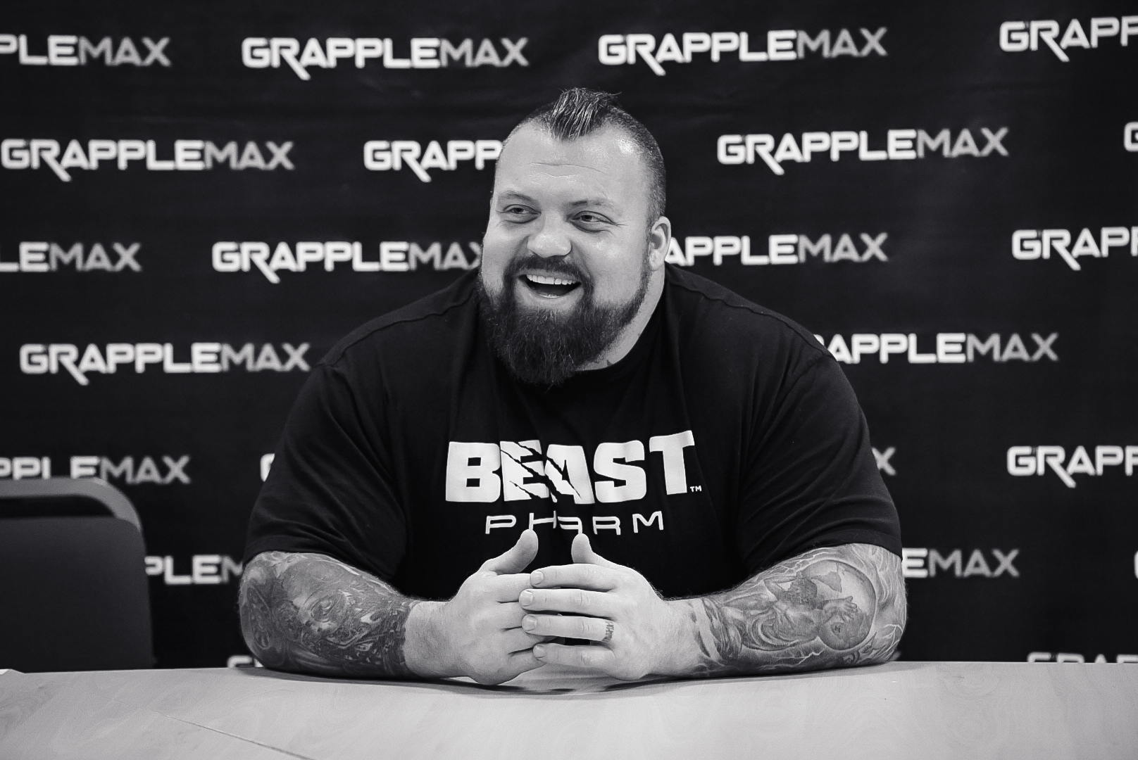 World's Strongest Man Eddie Hall as a special VIP guest at GrappleMax, smiling at a GrappleMax branded press table