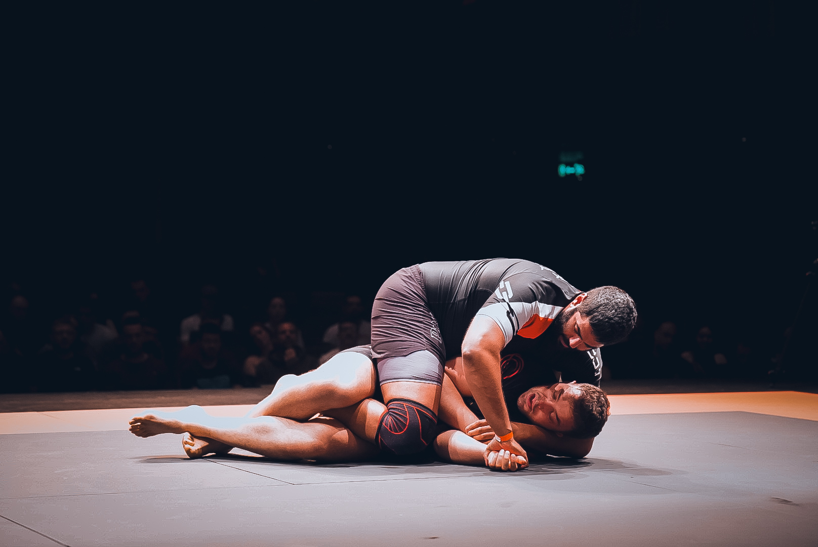 Two GrappleMax competitors in live action under the Theatre Severn lights, side control pressure with the crowd watching